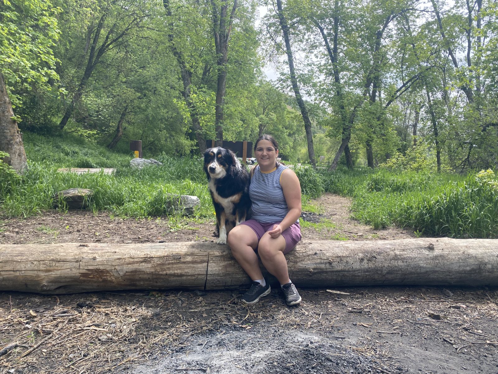Lillie and a dog resting together on a fallen log at the trailhead
