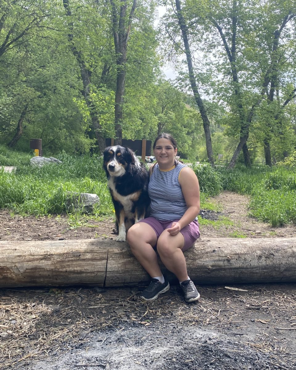 Portrait of Lillie sitting with a dog on a log at a Cache Valley trailhead