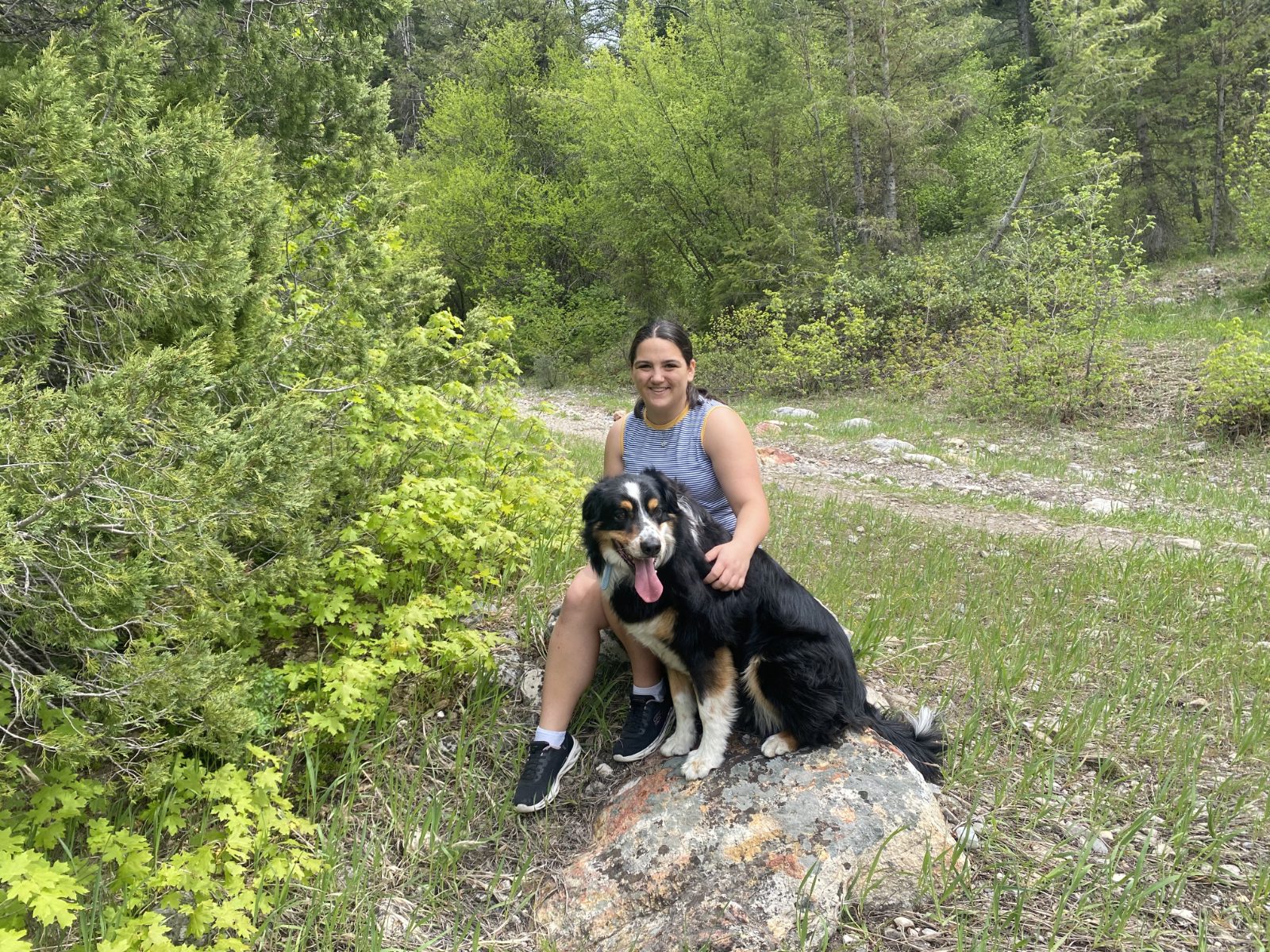 Lillie smiling beside a happy Australian Shepherd on a rock in the canyon