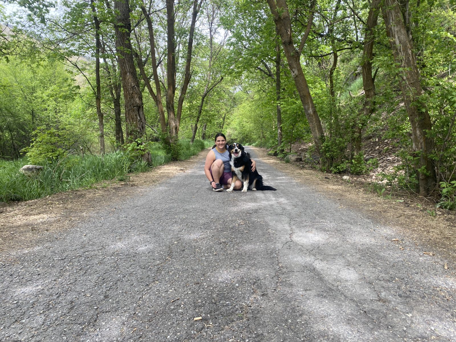 Lillie crouching with a dog on a tree-lined Cache Valley trail road